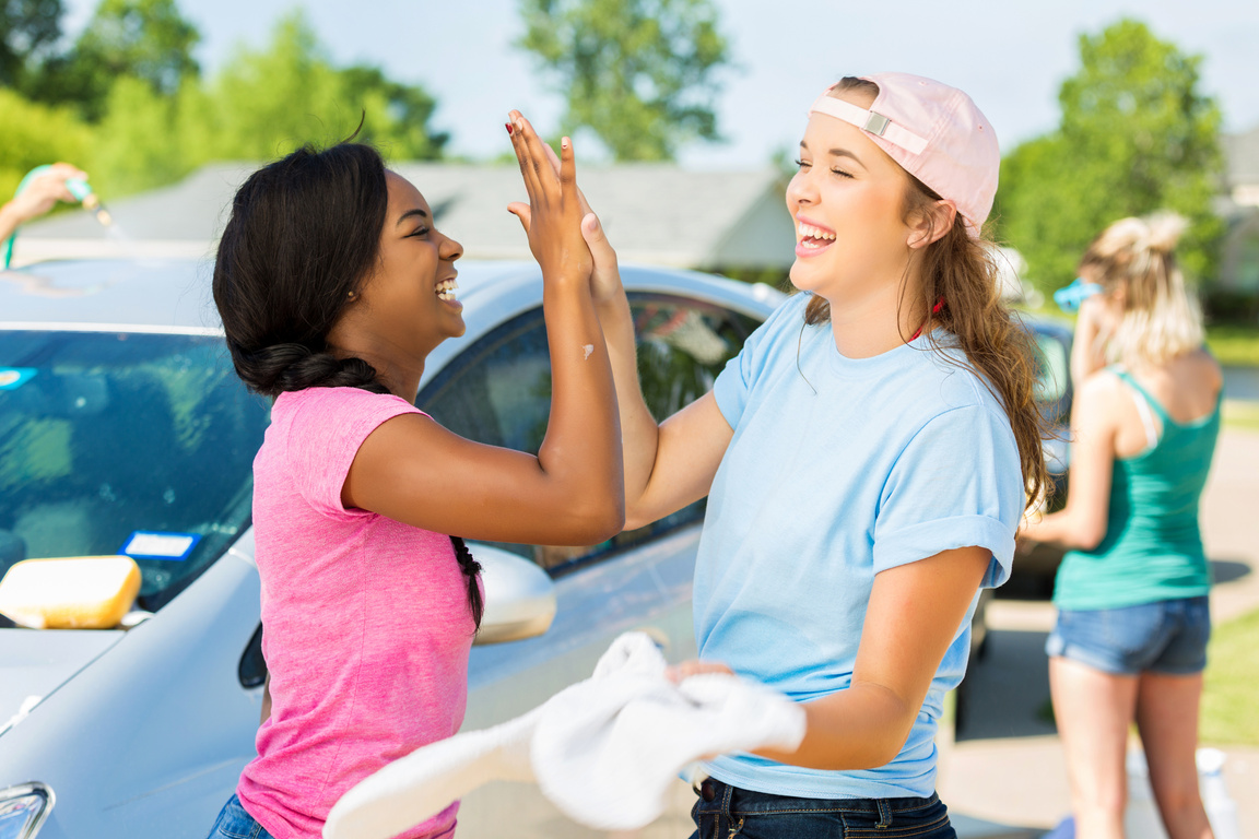 Friends give high fives while washing cars at fundraising event